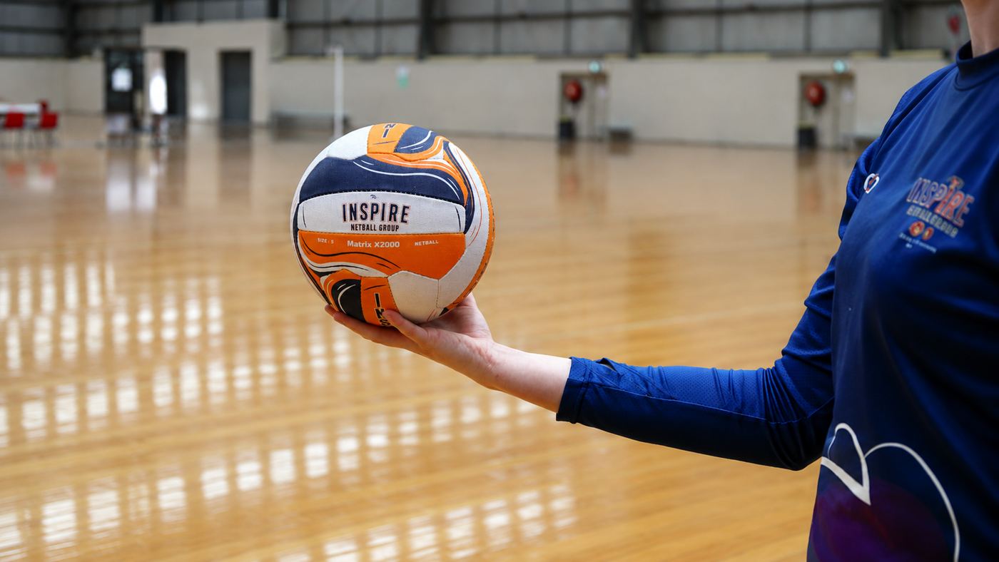 Inspire coach holding an Inspire Netball Group match ball on court